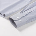 Close-up of FAHIZO Mens Dress Shirt, Regular Fit, light blue with a subtle checkered grid pattern and white buttons. The long sleeves are buttoned at the cuffs, highlighting the breathable stretch fabric laid flat on a white surface.