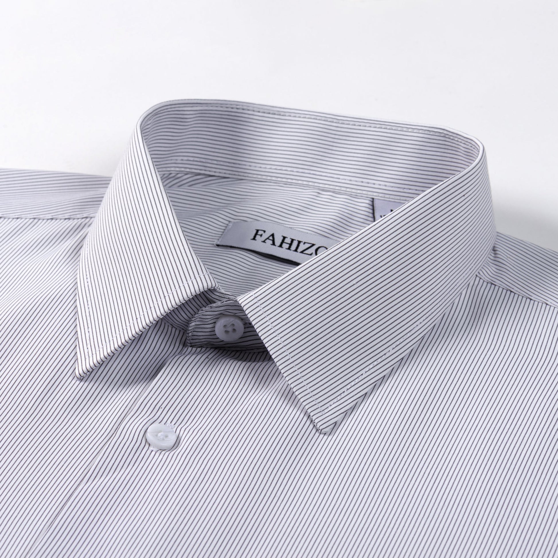 A close-up of a neatly folded FAHIZO Mens Dress Shirt Regular Fit Casual Long Sleeve, light-colored with fine black pinstripes, pointed collar, white buttons, and the FAHIZO label visible inside the collar.